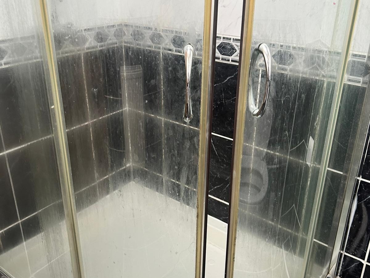 Shower enclosure with limescale-clouded glass doors before cleaning