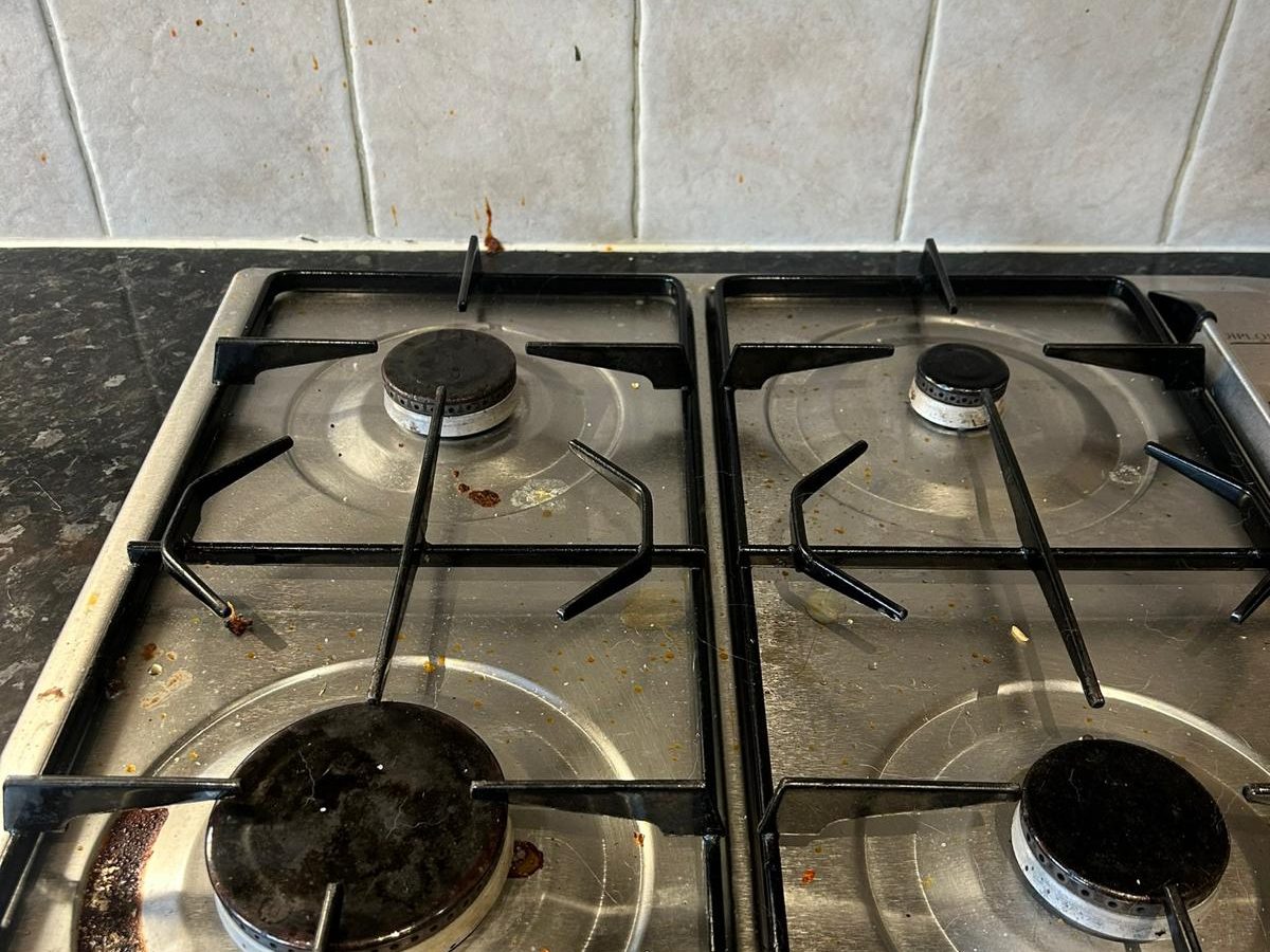 Gas hob with burnt-on spills and food debris before cleaning